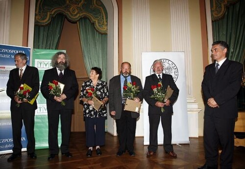 Pięć osób (pośrodku kobieta) trzymających w rękach dyplomy i kwiaty pozujących do zdjęcia. Z boku stoi mężczyzna - prezes IPN