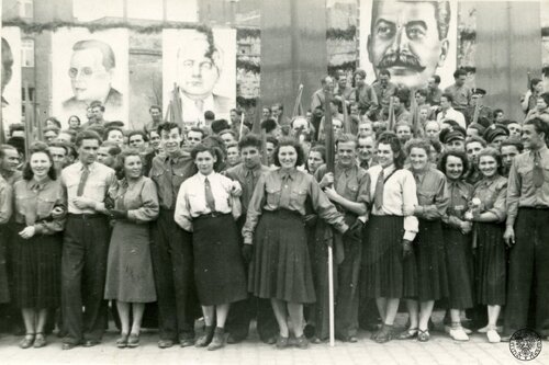 W tle widoczny jest portret Józefa Stalina i przypuszczalnie przywódców komunistycznych. Drugi od lewej to prawdopodobnie Wilhelm Pieck, przywódca Niemieckiej Republiki Demokratycznej w latach 1949 - 1960