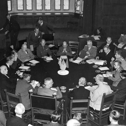 Rozmowy toczone przy okrągłym stole z udziałem prezydenta USA Harry’ego Trumana, sowieckiego dyktatora Józefa Stalina i premiera Wielkiej Brytanii Winstona Churchilla. Na środku stołu chorągiewki tych państw.