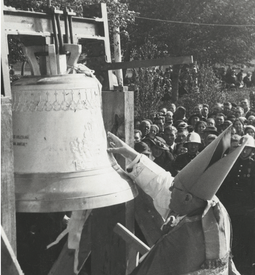 Hierarcha rzymskokatolicki trzyma prawą dłoń na dużym dzwonie