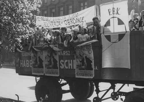 Tydzień Polskiego Białego Krzyża w Warszawie, 15 maja 1938 r. Samochód propagandowy udekorowany plakatami promującymi działalność Polskiego Białego Krzyża. Na platformie pojazdu młodzież.