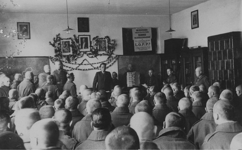 Odczyt w więzieniu Wojskowym Więzieniu Śledczym w Krakowie, zorganizowany przez Oddział Polskiego Białego Krzyża w Krakowie. Więźniowie zgromadzeni w sali wysłuchują przemówienia osoby stojącej pod ścianą z patriotyczną dekoracją - świetlica.