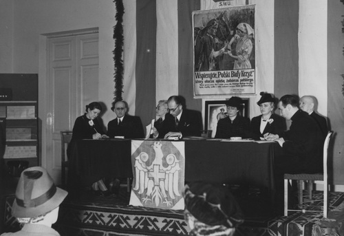 Prezydium Walnego Zjazdu Delegatów i Kół Polskiego Białego Krzyża w Kasynie Garnizonowym w Warszawie, 2 grudnia 1938 r. W środku przewodniczący Zjazdu prokurator Turski. Za członkami Prezydium plakat z hasłem wzywającym do wsparcia Polskiego Białego Krzyża.