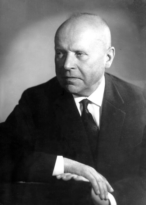 Stanisław Lorentz, profesor, historyk sztuki. Fotografia portretowa z profilu mężczyzny gładko ogolonego, łysiejącego, w ciemnej marynarce, białej koszuli, ze starannie zawiązanym krawatem.