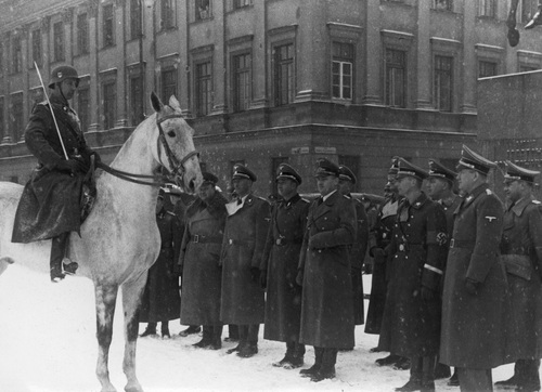 Gubernator Hans Frank (w pierwszym rzędzie trzeci z prawej) w trakcie wizyty w okupowanej Warszawie przyjmuje na placu Saskim defiladę szwadronu SS - marzec 1940 r. Widoczni również: Hermann Fegelein (z lewej obok Hansa Franka), Ludwig Fischer (pierwszy z prawej), Josef Friedrich Buhler (w drugim rzędzie drugi z prawej), Arthur Seyss-Inquart (w okularach) i Otto von Wachter (piąty z prawej w pierwszym rzędzie). Fot. NAC