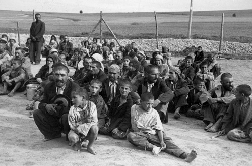 Grupa Cyganów w obozie siedzi na ziemi.