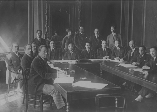 Grupa mężczyzn zasiadająca za stołami wewnątrz pomieszczenia, w którym odbywają się obrady.