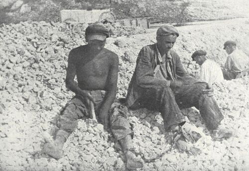 Więźniowie siedzący na zwałach kamieni.