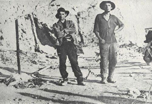 Dwójka więźniów pozujących do zdjęcia, prezentuje nogi skute u kostek łańcuchami.