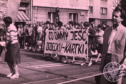 Manifestacja zorganizowana przez Zarząd Regionu Ziemi Łódzkiej NSZZ „Solidarność” – „Marsz głodowy kobiet”. Kobiety niosą transparent. U dołu i góry obrazu mężczyźni zabezpieczają marsz niosąc linę rozciągniętą wzdłuż ulicy Piotrkowskiej. Autor: nieznany, Łódź 30 lipca 1981 r. Fot. AIPN