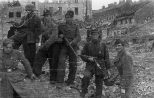 Grupa żołnierzy z bronią w ręku wśród ruin zabudowy miejskiej.