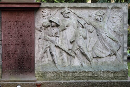 Fragment kamiennego pomnika cmentarnego, na którym uwidocznione są postaci polskich żołnierzy - ochotników w boju: dowódcy - generała Józefa Hallera, piechurów oraz kobiety i dwójki młodych chłopców. Obok przebiega inskrypcja: „[krzyż Chrystusowy] ORLĘTOM POLSKIM POLEGŁYM W OBRONIE WARSZAWY PODCZAS NAJAZDU BOLSZEWICKIEGO ROKU 1920 WDZIĘCZNI RODACY”.