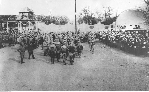 Grupa umundurowanych mężczyzn, ustawiona w trójki i czwórki, gotowa do wymarszu (zdjęcie zrobione "od tyłu")