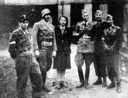 Niewyraźne zdjęcie sześciu osób pozujących do zdjęcia. Trzecia od lewej stoi kobieta, pozostałe postaci to mężczyźni w mundurach.