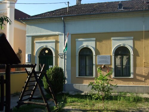Fragment zabudowy z widocznymi elementami drewnianej małej architektury placu zabaw. Na budynku widoczna flaga Węgier