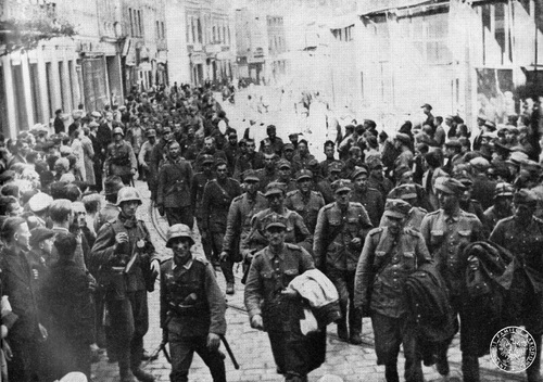 Kolumna polskich jeńców z Armii „Pomorze” prowadzonych ulicą zajętego przez Niemców Grudziądza, 5-6 września 1939 roku. Przy kolumnie śmiejący się żołnierze niemieccy oraz milczący, przypatrujący się przemarszowi cywile.
