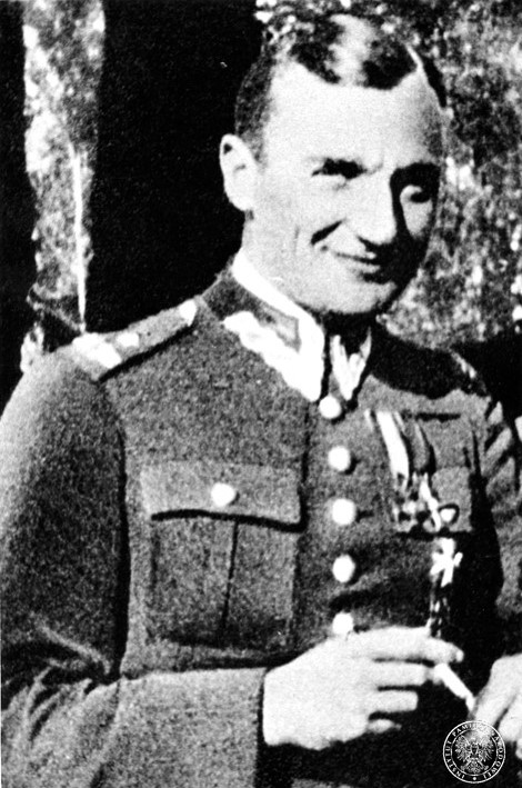 Mjr Dobrzański jest uśmiechnięty; ma na sobie mundur; po lewej stronie klatki piersiowej przypięte odznaczenia wojskowe, włosy zaczesane do góry na prawą stronę. W dłoniach trzyma papierosa