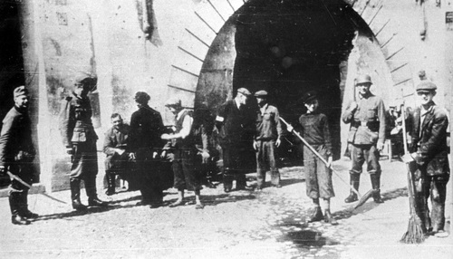 Żydzi przy pracy na jednej z ulic okupowanej przez Niemców Warszawy w czasie II wojny światowej. Niemieccy funkcjonariusze pozują do zdjęcia z represjonowanymi ludźmi. Fot. NAC