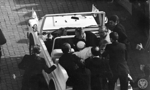 13 maja 1981, zamach na papieża Jana Pawła II. Odjazd papamobile z rannym Ojcem Świętym, podtrzymywanym przez ks. Stanisława Dziwisza, w kierunku Watykanu. Z tyłu samochodu oraz wokół niego papieska ochrona. Fot. z zasobu IPN