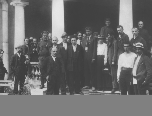 Delegaci na Drugi kongres Kominternu. Wśród kolumnady, na schodkach, stoi grupa osób, głównie mężczyzn, w różnym wieku i różnie ubranych - w garnitury z krawatami, bez krawatów, same koszule; parę osób ma na sobie ubrania typu wojskowego. Na pierwszym planie - Lenin.