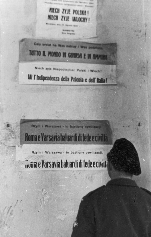 A soldier of the 2nd Independent Armoured Brigade in front of a wall with welcoming posters for Poles in Italy, 1944. Photo: NAC Slogans on the wall say: <i>Long live Poland! Long live Italy!; The entire World looks at you and admires you; Long live the independence of Poland and Italy!; Rome and Warsaw are bastions of civilisation</i>