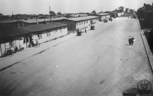 Widok na baraki i plac apelowy po wyzwoleniu KL Mauthausen. Na szerokiej alei obozu oraz pod ścianami baraków przebywają pojedyncze osoby.