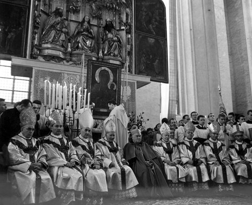 Biskupi w szatach liturgicznych siedzący w rzędzie przed ołtarzem głównym, przed którym ustawiono obraz z jasnogórskim wizerunkiem Matki Bożej.