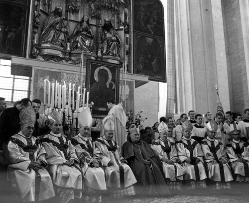 Biskupi w szatach liturgicznych siedzący w rzędzie przed ołtarzem głównym, przed którym ustawiono obraz z jasnogórskim wizerunkiem Matki Bożej.