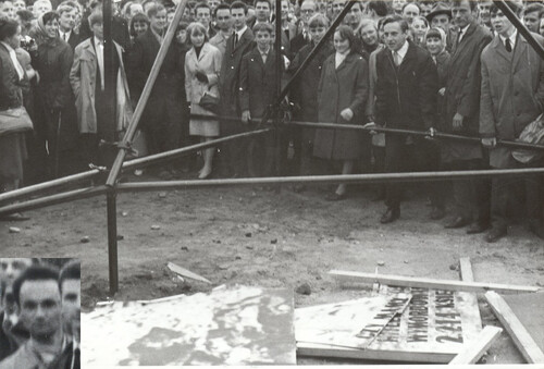 Ludzie skupieni wokół metalowej konstrukcji. Mężczyzna wykonując ruch, trzyma rękoma element konstrukcji.