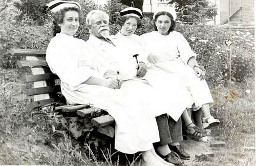 Mężczyzna siedzący na ławce w białym fartuchu lekarskim w otoczeniu trzech kobiet w białych fartuchach i pielęgniarskich czepkach