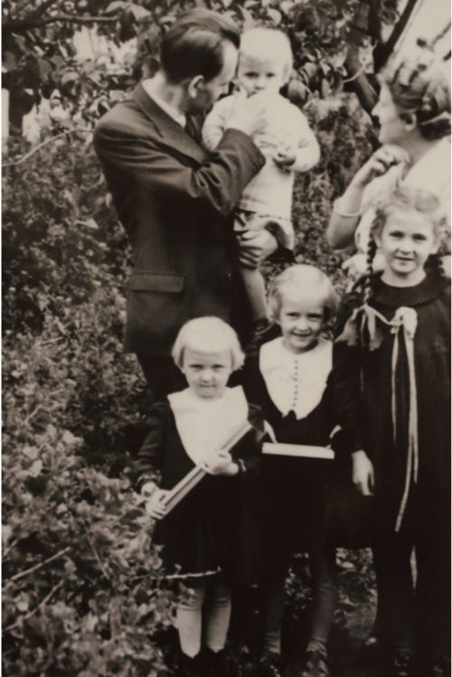Rodzinna fotografia. Małżeństwo i stojące przed nimi trzy dziewczynki, meżczyzna trzyma w ręku niemowlę
