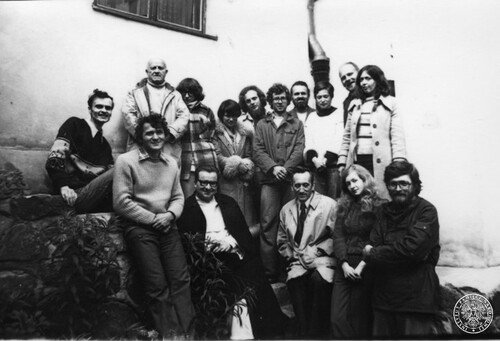 Pozowane zdjęcie dużej grupy osób, kobiet i mężczyzn, stojących w dwóch rzędach przy murze budynku.