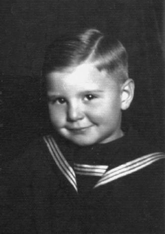 Fotografia portretowa chłopca o szerokim, dziecięcym uśmiechu, pucułowatych policzkach, gładko zaczesanych włoskach, ubranego w dziecięcy strój marynarski.