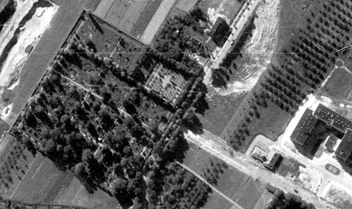 Zdjęcie lotnicze cmentarza w Wieluniu z 1956 r. Alejki cmentarne wśród drzew. Teren cmentarza odgrodzony. Wokół pola i pojedyncze budynki.