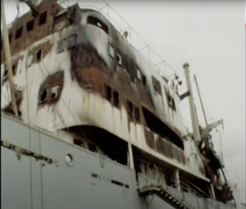 Zabudowania nad pokładem statku z widocznymi zniszczeniami i nadpaleniami