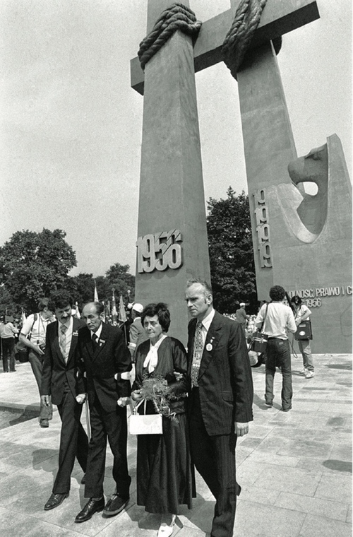 Trzech mężczyzn i kobieta stoją przed pomnikiem z napisem &amp;quot;1956&amp;quot;, kobieta trzyma w ręku wiązankę