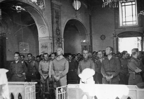 Nierozpoznana uroczystość w 6 Lwowskiej Brygadzie Piechoty (1944-1946 r.). Płk Witold Nowina-Sawicki stoi wśród żołnierzy zgromadzonych we wnętrzu świątyni w trakcie nabożeństwa. Budowla nosi ślady zniszczeń, m.in. duża wyrwa w sklepieniu nawy bocznej.