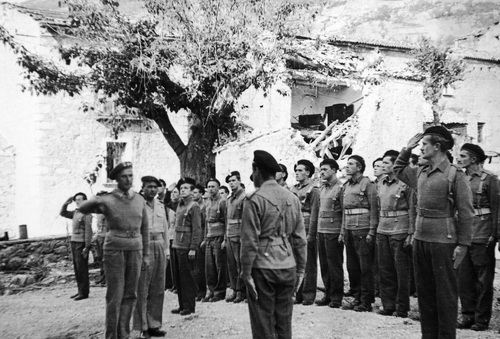 Nierozpoznana uroczystość w 6 Lwowskiej Brygadzie Piechoty (1944-1946 r.). Płk Witold Nowina-Sawicki stoi przed oddziałem żołnierzy zgromadzonych na niewielkim placu. W tle ściana niskiego budynku i drzewo.