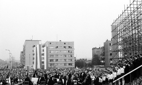 Ceremonia odsłonięcia Czerwcowej tablicy pamiątkowej przed bramą główną HCP, 27 czerwca 1981 r. Licznie zgromadzeni uczestnicy uroczystości w przestrzeni wśród budynków. Na pierwszym planie chór i orkiestra. W głębi, m.in. pionowe, biało-czerwone banery.
