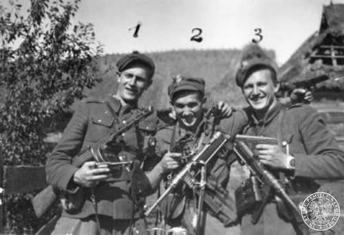 Trzech uśmiechniętych mężczyzn, w mundurach i z karabinami, pozujących do zdjęcia