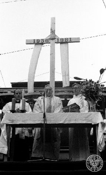 Ołtarz polowy, nad którym góruje wysoki, przepasany wielką stułą, krzyż z datami rocznymi „1956 1981”. Prze stołem ofiarnym stoi trzech księży katolickich w szatach liturgicznych odprawiających Mszę świętą.