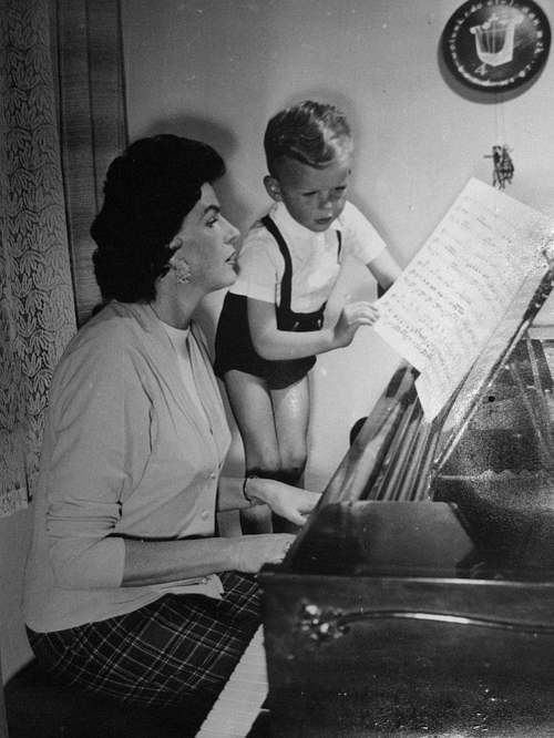 Maria Koterbska z synem Romanem. Kobieta siedzi przy pianinie, chłopiec przewraca kartkę z nutami.