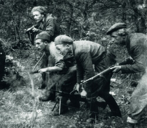 Patrol dywersyjny z Obwodu Armii Krajowej Łańcut w terenie leśnym. Czterech mężczyzn, w pochylonych pozycjach, ubranych w cywilne ubrania, idzie trzymając w rękach broń przygotowaną do użycia.