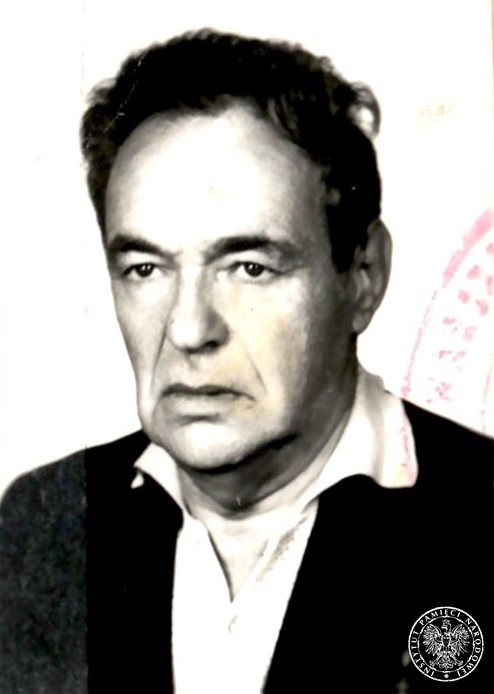 Zdjęcie portretowe Maksymiliana Sznepfa. Starszy mężczyzna o pociągłej twarzy, obwisłych policzkach, wysokim czole i ciemnych włosach, gładko ogolony, ubrany w marynarkę lub sweter i białą, rozpiętą pod szyją koszulę.