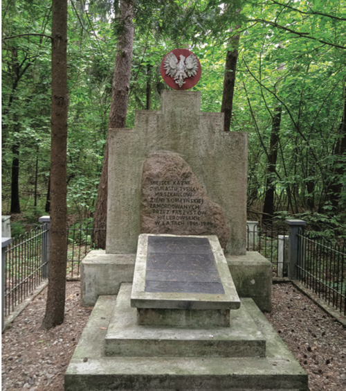 Leśny pomnik z tablicą (z motywem orła białego) i głaz narzutowy.