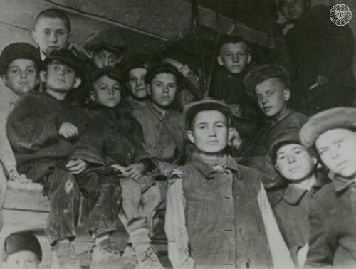 Dzieci polskie - po straszliwych doświadczeniach zgotowanych im przez Związek Sowiecki po agresji na Polskę 17 września 1939 roku - ewakuowane z „nieludzkiej ziemi” do Persji. Pomieszczenie, prawdopodobnie wagonu. Grupa chłopców, bardzo skromnie, wręcz nędznie, ubranych, siedzi i stoi w paru rzędach. Wzrok chłopców jest pełen dramatyzmu po przebytych doświadczeniach, na twarzach kilku rysuje się wciąż żywe przerażenie.