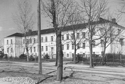 Busko Zdrój, 1942 rok - okupacja niemiecka. Fragment ulicy z budynkiem okupacyjnego niemieckiego starostwa powiatowego - widok zewnętrzny jasnego, długiego, piętrowego gmachu; przed nim pojedyncze drzewa.
