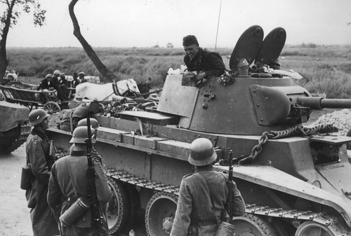 Sowiecki czołgista z pojazdu bojowego BT-7 prowadzi rozmowę z grupą niemieckich żołnierzy na linii demarkacyjnej, dzielącej najechane przez agresorów ziemie Polski we wrześniu 1939 r. Widoczny zarys kolejnego czołgu. W tle wóz konny z ludnością cywilną. Dalej łąki.