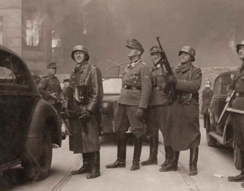 Jürgen Stroop (pośrodku, w czapce polowej) w płonącym getcie warszawskim, kwiecień 1943 r. Grupa niemieckich oficerów i żołnierzy w trakcie powstania w getcie w Warszawskim. Pośrodku, patrzący w górę, SS- Brigadeführen Jurgen Stroop. Za jego plecami najprawdopodobniej SS-Rottenfuhrer Josef Bloshe. Obok nich stoją żołnierze uzbrojony w pistolety maszynowe. W tle płonące budynki. Zdjęcie pochodzące z raportu Jurgena Stroopa dla Heinricha Himmlera (orginalnie zatytułowane &quot;Dowódca wielkiej operacji&quot;).