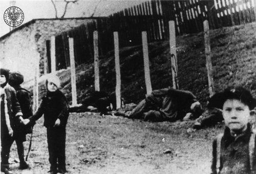 Dzieci na miejscu egzekucji osób rozstrzelanych w Tomaszowie Mazowieckim przy ulicy Browarnej, listopad 1943 r.  Troje dzieci, za nimi zwłoki rozstrzelanych skazańców w egzekucji.